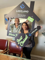 Couple posing for a photo while the woman holds a large key cut out and the man is holding up a large house cut out with a hole of which his torso and head is peeking through.