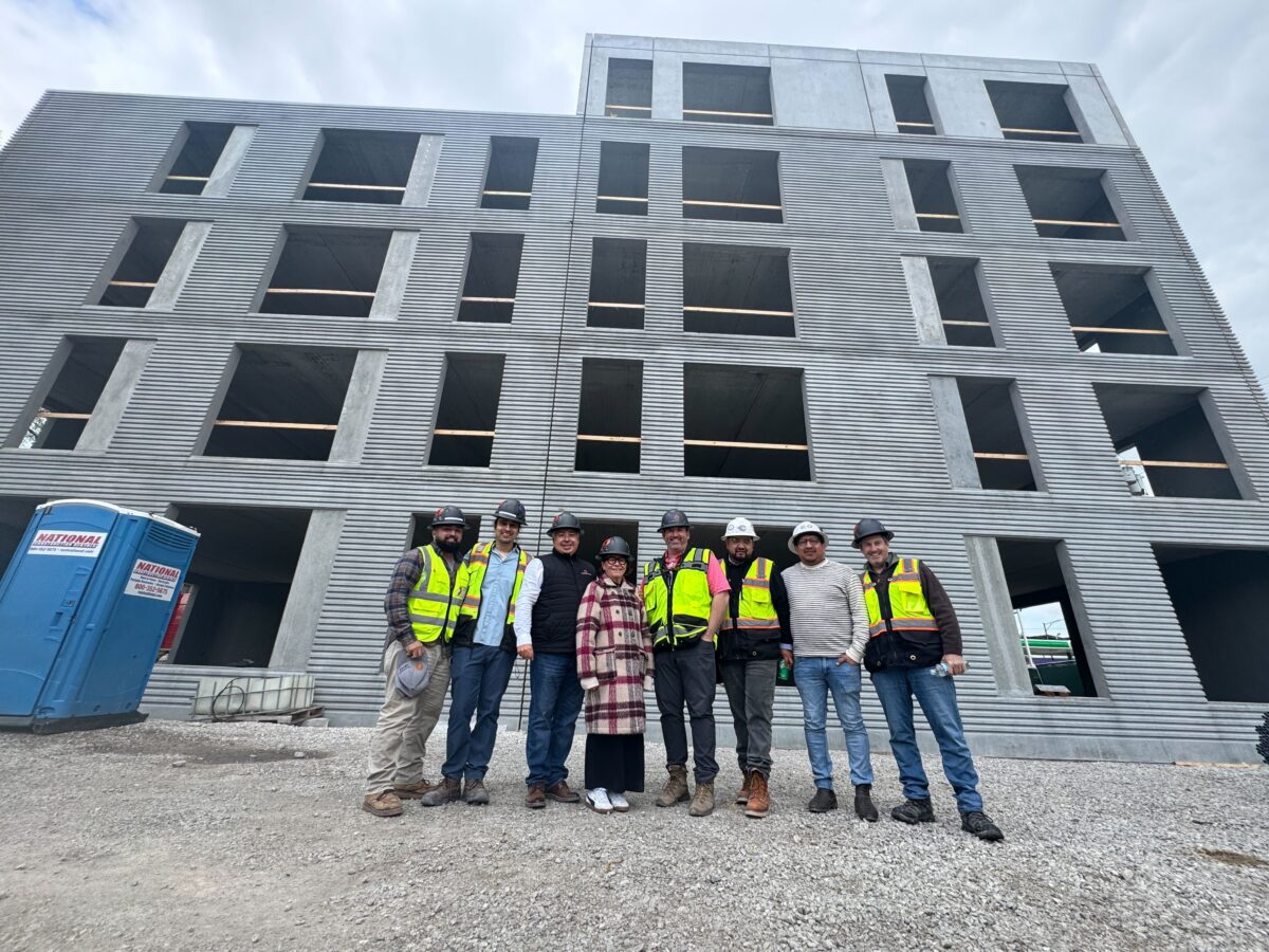 Staff and crew, some with construction vests, standing if front of a development construction of a new building.