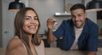 Couple taking a selfie while husband holds keys while leaning over a kitchen counter.
