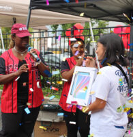 Prize winner holding a tablet package while pastel colored confetti showers the participant. She is joined by TRP staff wearing red jerseys.